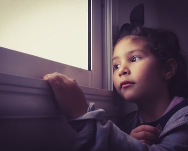 niña sola en casa mirando por una ventana
