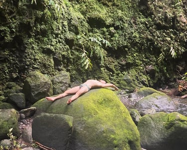 man laying on the rocks under a waterfall after a hike