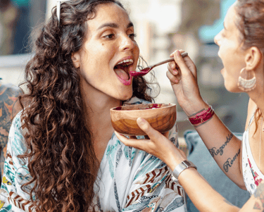a woman eating a bowl of food while a man is eating