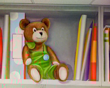 A painted bookshelf in trompe l'oeil style, showing a cute stuffed bear and fun colourful books