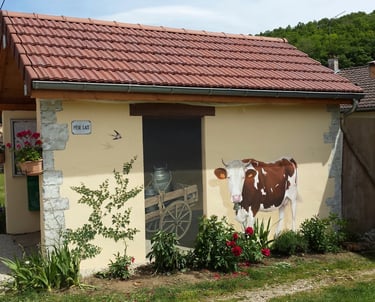 Fresque murale sur façade comporte une fausse porte, une vache et un lierre peints.