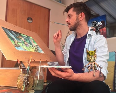 A handsome young male artist with dark hair and blue shirt sits at his easel of fantasy art