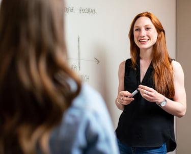 a woman in a black top and jeans standing in front of a white board