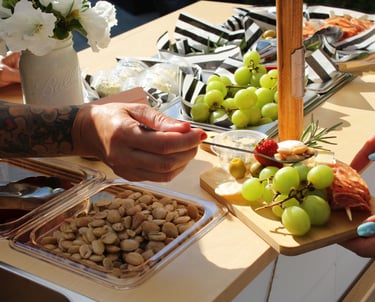 a person holding a charcuterie board over a bar cart with various foods in the background