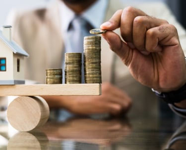 a man in a suit and tie is holding a house on a scale with coins