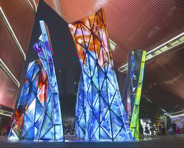 Blooming Sculpture lit up at night with its multi-colored glass panels and people walking around it