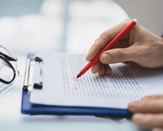 A person holding a pen and writing on a paper representing editing and proofreading