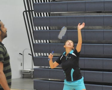 Ellen  preparing to serve during a badminton match in an indoor gym.