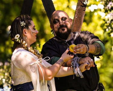 Pareja en ceremonia de boda medieval sonriendo y compartiendo un objeto amarillo en un bosque