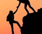 two people climbing a mountain at sunset