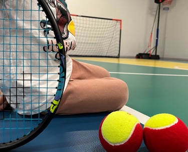 Primo piano di una racchetta da tennis e due palline rosse e gialle su un campo multisport nella palestra Move 2 Grow a Milan