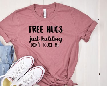A pink t-shirt, jeans and sneakers. The t-shirt reads "Free Hugs - just kidding - don't touch me"