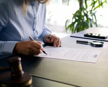 Manos firmando un documento en el escritorio con lupa y carpeta.”
