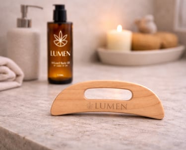Wooden gua sha massage tool and Lumen infused body oil on a marble spa counter with a candle.