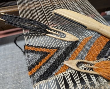 a weaving loom with shuttle, combe and black grey orange wool threads on a navajo rug in progress