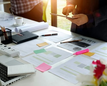 Project charts spread out on a desk with Post-It Notes and markets