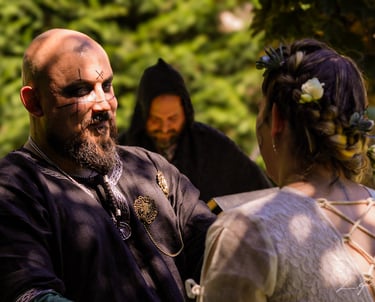 Hombre con maquillaje y tatuajes faciales vestido con traje medieval oscuro, mirando a su pareja dur