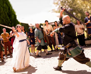 Pareja de novios con vestimenta medieval, ella con vestido blanco y él con traje verde, bailando y l
