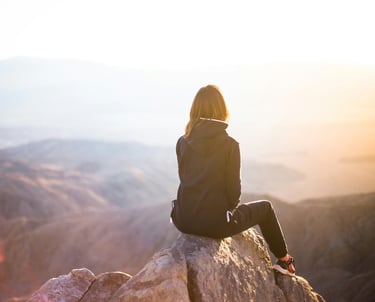 Solo traveler seated on a mountaintop, gazing at a serene sunset view.