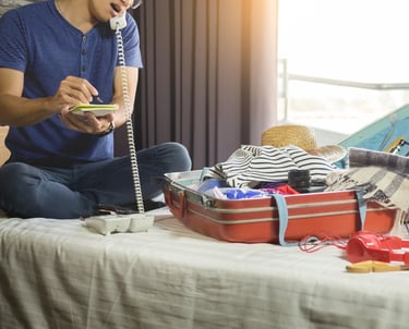 a man sitting on a bed with a suitcase and a phone
