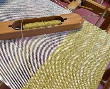 a weaving loom with shuttle and olive green threads on a 4 harness textile in progress