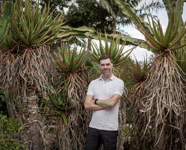 Man stands in a lush botanical garden surrounded by tall aloe and cactus plants, Madeira lifestyle and natural greenery.