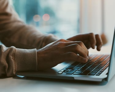 Person with beige sweater typing on a laptop symbolizing meaningful obituary services.