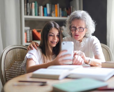 a woman and a young girl are sitting at a table looking at phone.