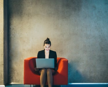 A woman sitting on a red chair with a laptop