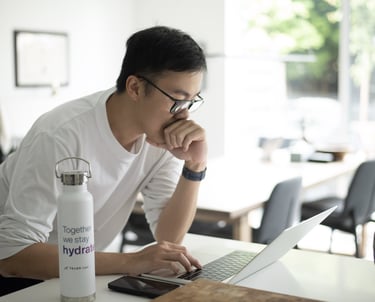 a man sitting at a table with a laptop and a water bottle