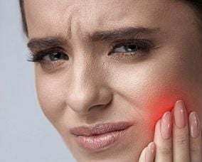 Mulher com a mão no rosto ilustrando sintomas de bruxismo avaliados por dentista na Lapa PR.