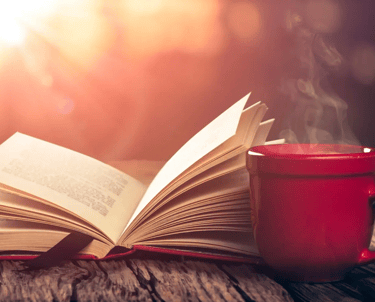 A book and cup of coffee on a table outside.