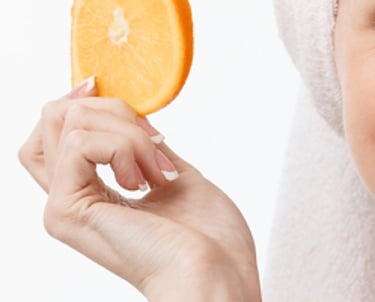 Vrouw met handdoek op haar hoofd en een appelsien voor haar ogen