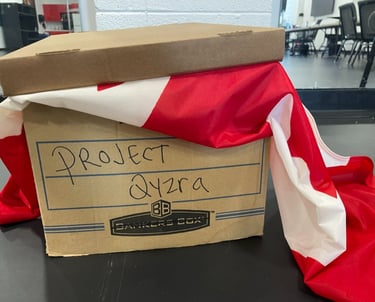 A cardboard file box with Project Qyzra written on it and a Canadian flag sticking out under the lid