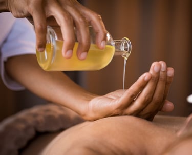 Thai aroma massage. A masseuse pores oil from into her hand above the bare back of a lady
