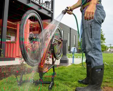 A bike flipped upside down, on the grass, with someone next to it spraying it with a hose