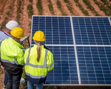 Fotografía de dos hombres y una mujer con cascos de protección color amarillo frente a paneles solar
