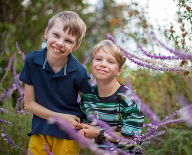 Two brothers share a happy moment surrounded by purple wildflowers in Pestana Grand, Madeira, natural lifestyle family photo.