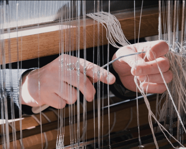 A person inserts the warp threads through metal eyelets of the harnesses
