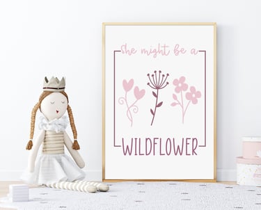 Framed wall art surrounded by a princess doll and pink accessories, with pink flowers & reads "She might be a Wildflower"