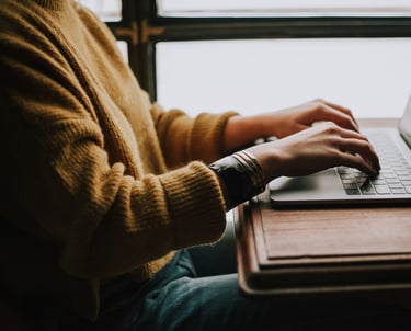 Photograph of a person sat at a desk with their hands on the keyboard of a laptop