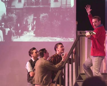 A male college student stands on the stairs in a frozen pose as an admirer sings about him.
