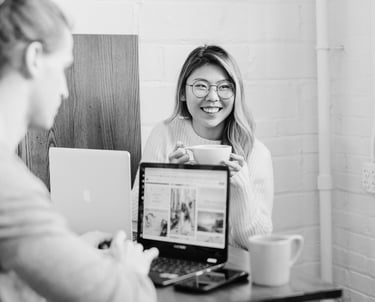 university students sitting at a desk working on their laptops and drinking coffee