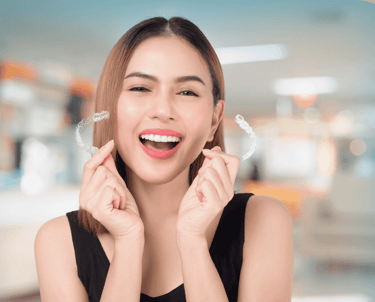 Mujer joven sonriente mostrando dos alineadores dentales transparentes de ortodoncia invisible