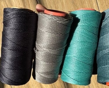 Cuatro bobinas de hilo de poliéster encerado de alta calidad en negro, gris, verde azulado y verde.