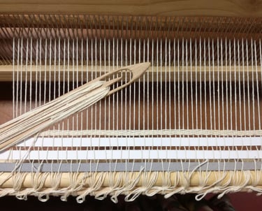 a weaving loom with a white cotton warp and a wooden shuttle with white cotton thread