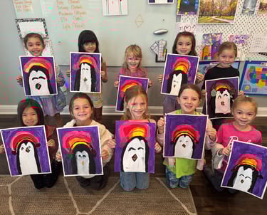 Kids proudly showing their penguin paintings from art classes at Kelley’s Neighborhood Art.