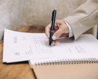 A woman's hand holding a pen and writing on an invoice on top of an open notebook