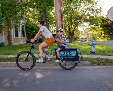 A mother riding her bike with a young boy sitting behind her on a rack