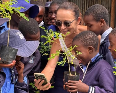 Young school children holding trees surrounding a teacher 